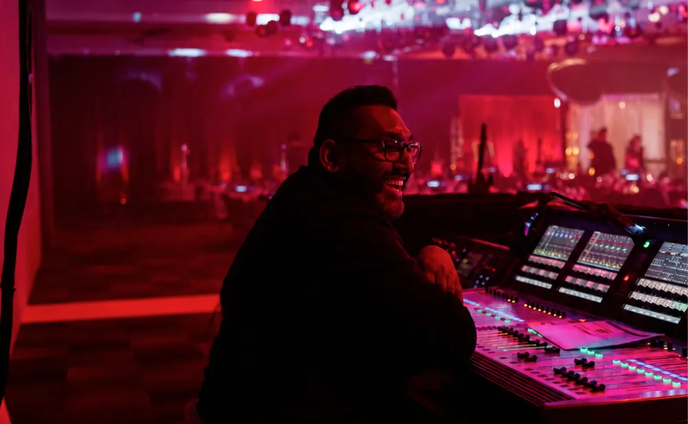 Event technician operating a control desk beside a red-lit ballroom.