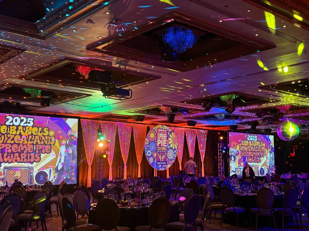 Awards dinner room filled with coloured lighting and large video screens.