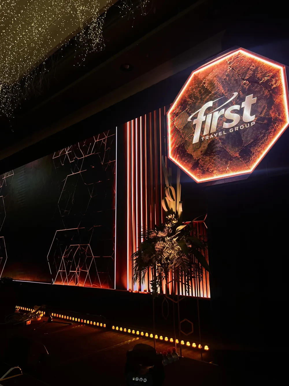 Illuminated event branding beside a stage edged with warm lighting.