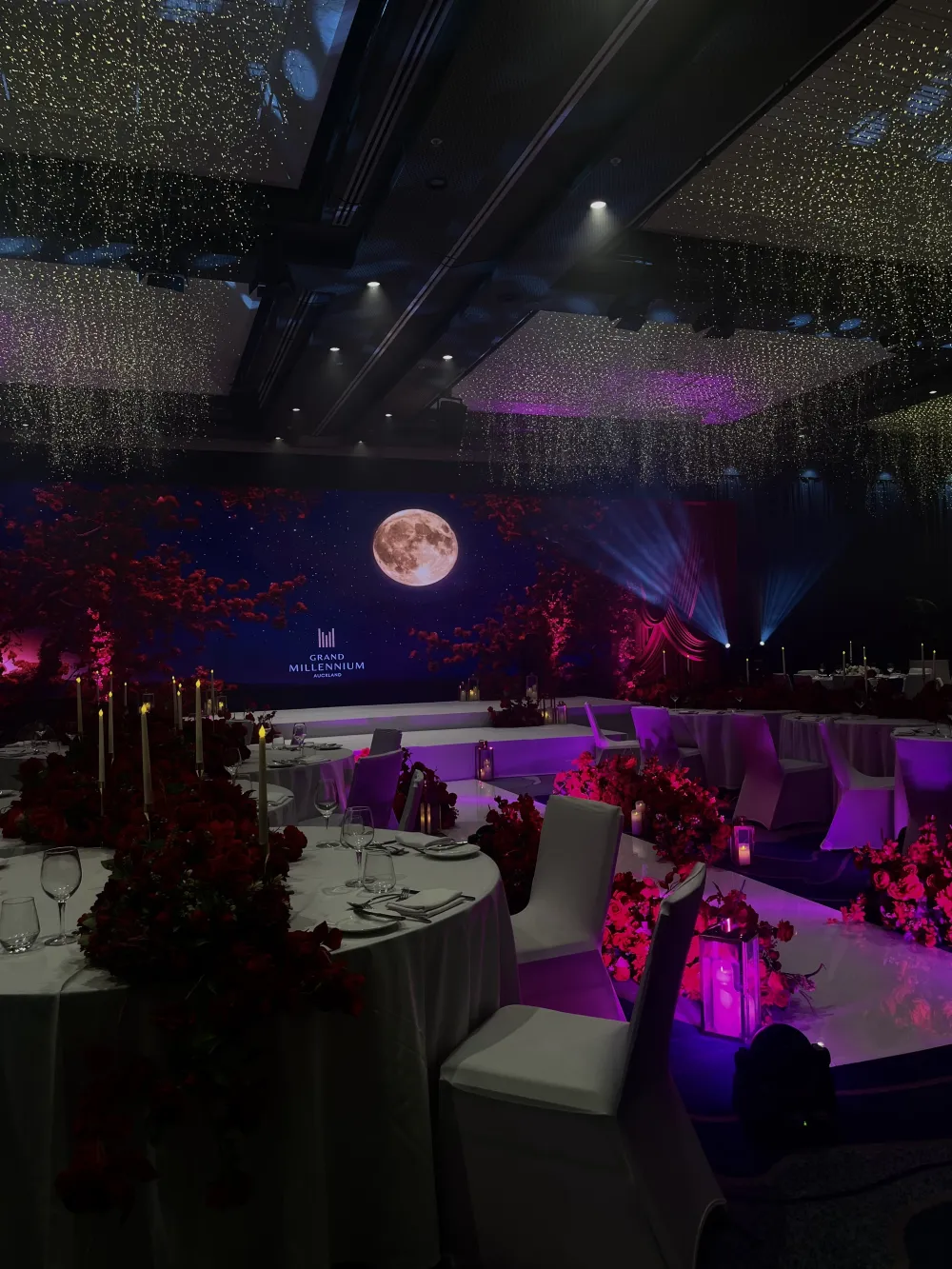 Gala dinner room with purple lighting and illuminated stage displays.