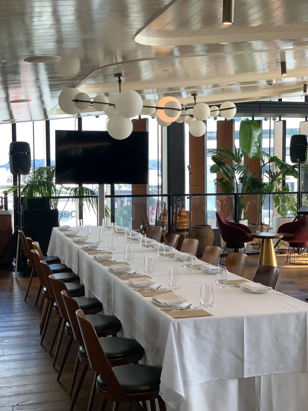 Long event tables facing a presentation screen in a window-lined dining room.