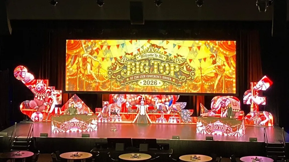 Gala dinner stage with a colourful carnival-themed screen and decorative figures.