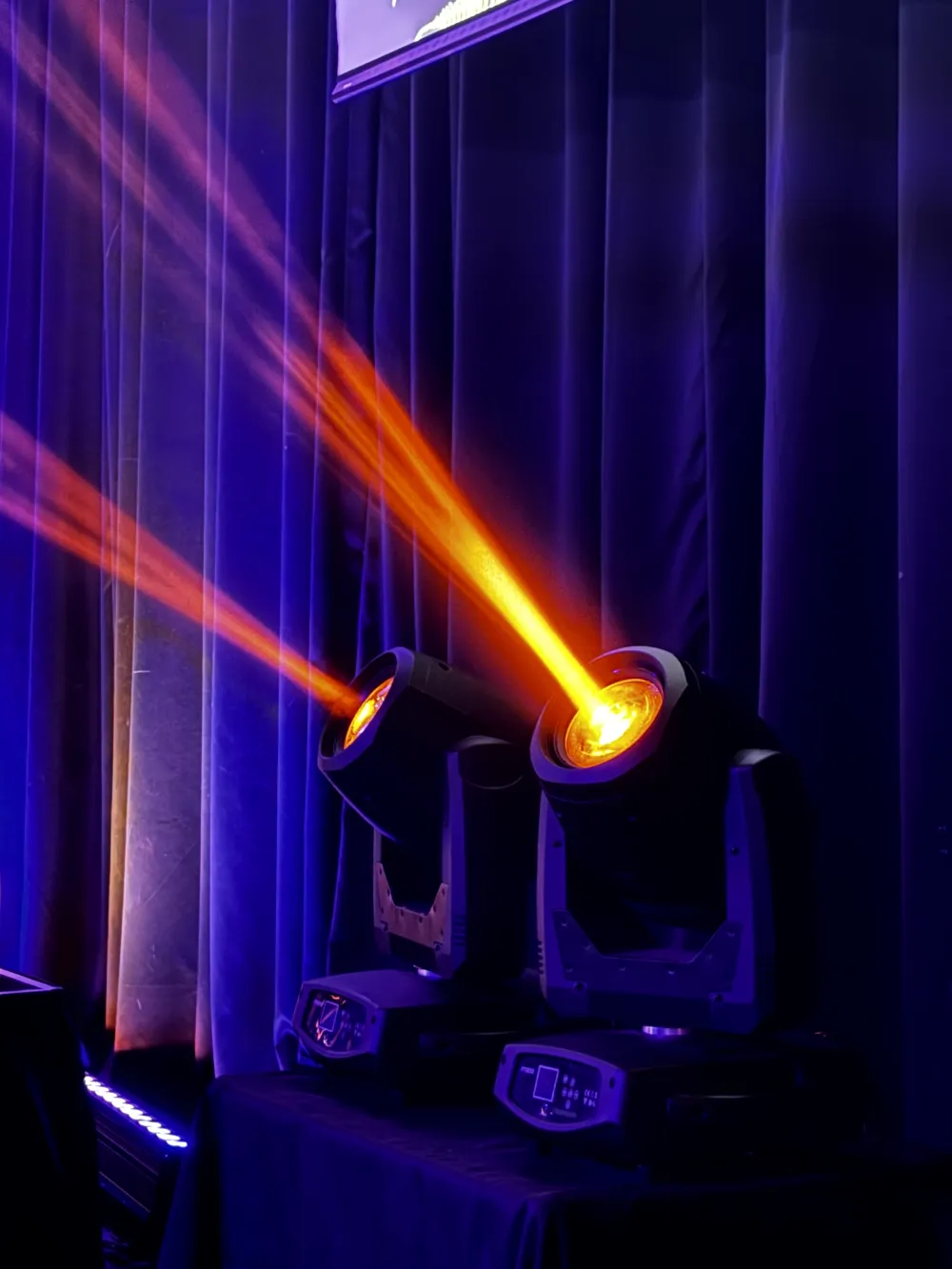 Moving-head lights projecting orange beams against blue curtains.