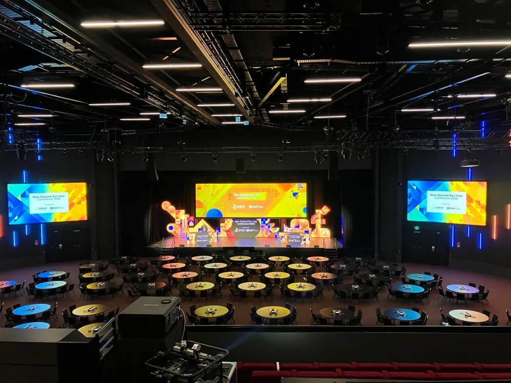 Stage with a central LED screen and two side screens overlooking banquet tables.